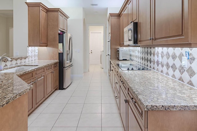 kitchen featuring tasteful backsplash, light stone countertops, light tile patterned flooring, stainless steel appliances, and a sink