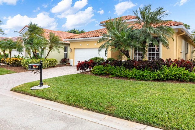 mediterranean / spanish-style home featuring a front lawn, a tile roof, stucco siding, decorative driveway, and a garage