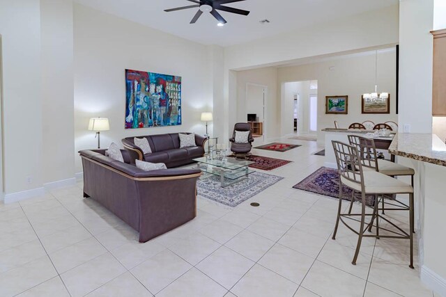 living room with light tile patterned floors, visible vents, baseboards, and ceiling fan with notable chandelier