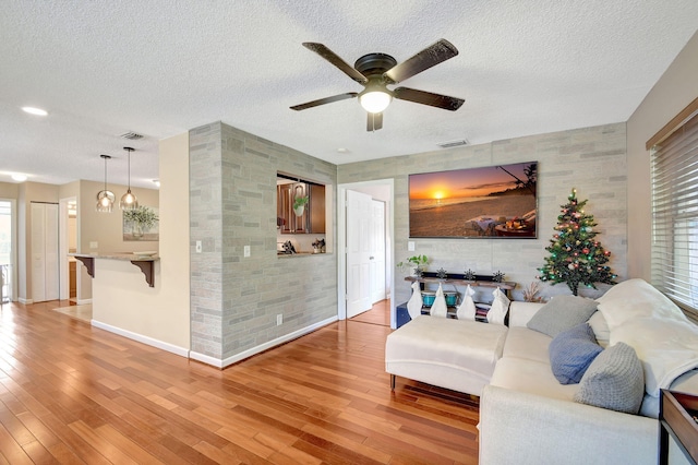 living room featuring ceiling fan, light hardwood / wood-style flooring, and a textured ceiling