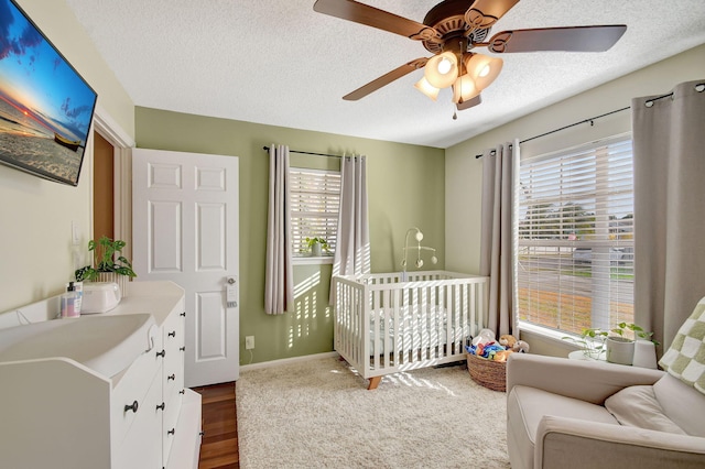 bedroom featuring a crib, multiple windows, hardwood / wood-style flooring, and ceiling fan