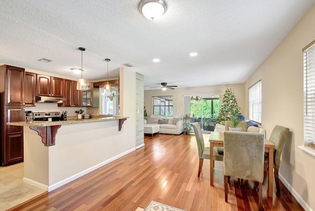 kitchen featuring light stone countertops, light wood-type flooring, a breakfast bar, ceiling fan, and stainless steel range oven