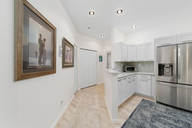 kitchen with backsplash, stainless steel appliances, white cabinetry, and light hardwood / wood-style flooring