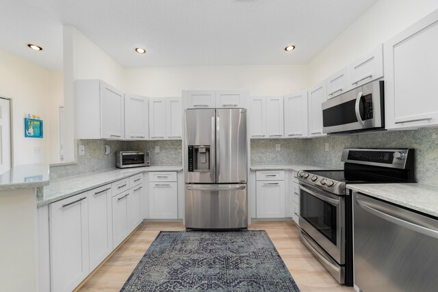 kitchen with decorative backsplash, light hardwood / wood-style floors, white cabinetry, and stainless steel appliances