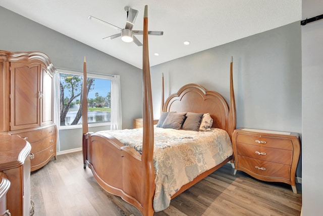 bedroom featuring light wood-type flooring, a water view, vaulted ceiling, and ceiling fan