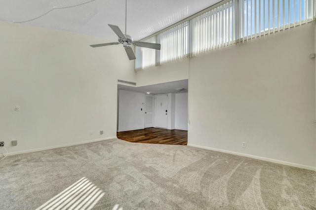 unfurnished living room with carpet, ceiling fan, and a high ceiling