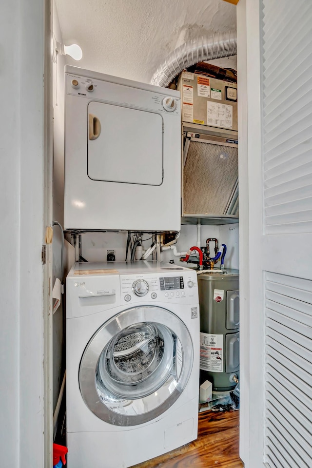 clothes washing area featuring a textured ceiling, electric water heater, stacked washer and clothes dryer, and wood-type flooring