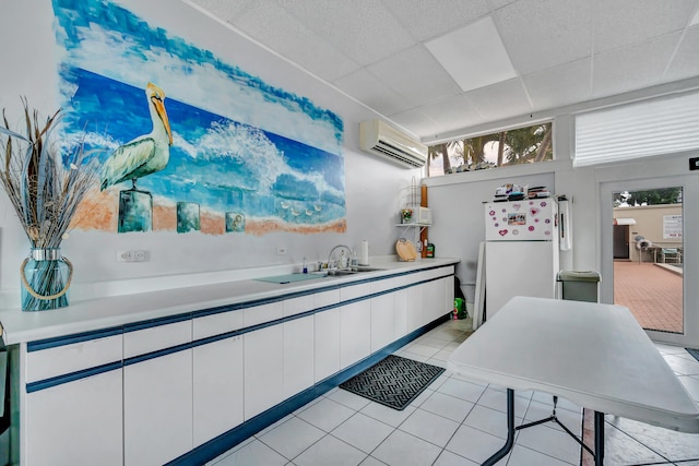 kitchen with a drop ceiling, an AC wall unit, white fridge, white cabinetry, and light tile patterned flooring