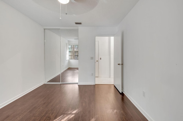 unfurnished bedroom with a closet, dark wood finished floors, visible vents, and baseboards