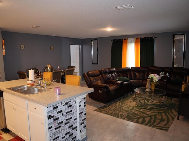 interior space with dishwasher, white cabinets, sink, light tile patterned floors, and an island with sink