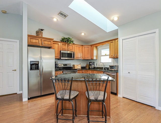 kitchen featuring vaulted ceiling with skylight, a center island, light wood-type flooring, and appliances with stainless steel finishes