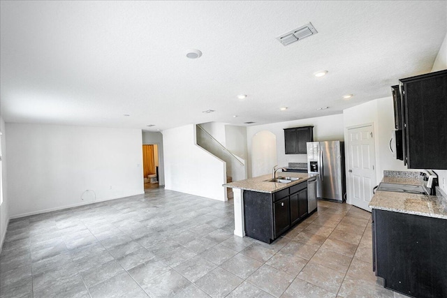 kitchen featuring a center island with sink, light stone countertops, sink, and appliances with stainless steel finishes