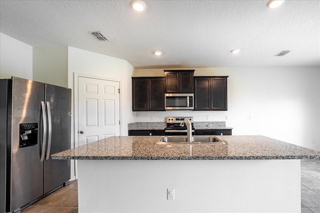 kitchen featuring a textured ceiling, stainless steel appliances, a kitchen island with sink, and sink