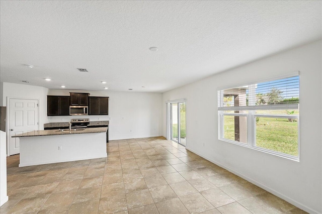 kitchen with a textured ceiling, sink, a kitchen island with sink, and appliances with stainless steel finishes