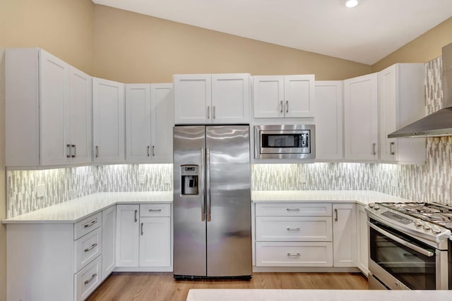 kitchen featuring vaulted ceiling, stainless steel appliances, decorative backsplash, and white cabinets