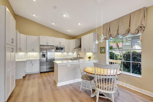 kitchen with stainless steel appliances, backsplash, decorative light fixtures, wall chimney range hood, and white cabinets