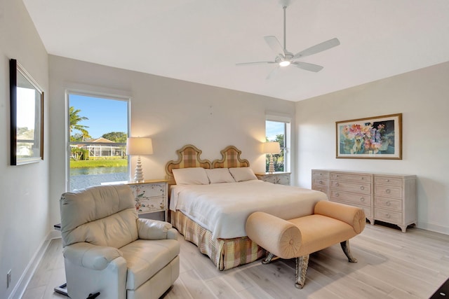 bedroom featuring ceiling fan, multiple windows, a water view, and light wood-type flooring