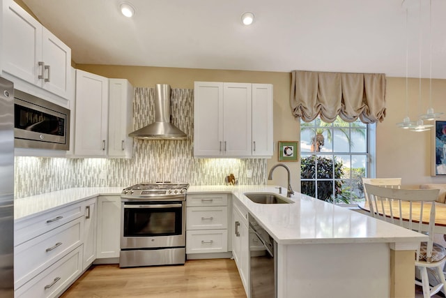 kitchen with kitchen peninsula, wall chimney exhaust hood, sink, and stainless steel appliances