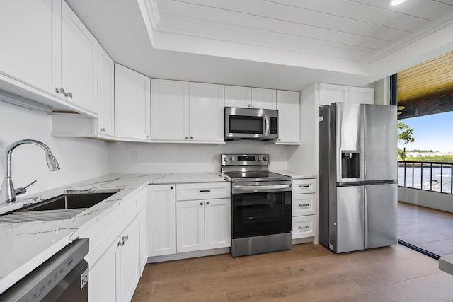 kitchen featuring appliances with stainless steel finishes, light stone counters, sink, white cabinets, and hardwood / wood-style floors