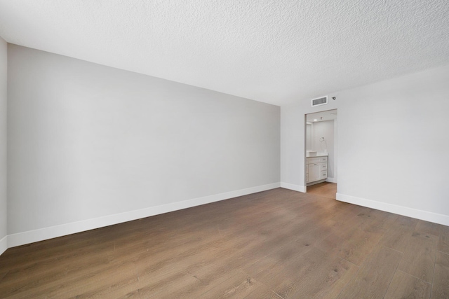 unfurnished bedroom featuring ensuite bathroom, dark hardwood / wood-style flooring, and a textured ceiling