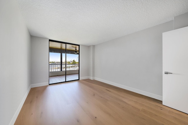 empty room with floor to ceiling windows, light hardwood / wood-style floors, and a textured ceiling