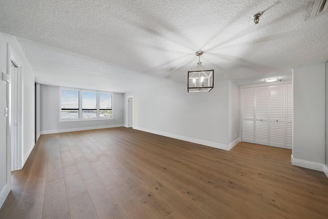 unfurnished living room with a notable chandelier, dark hardwood / wood-style flooring, and a textured ceiling