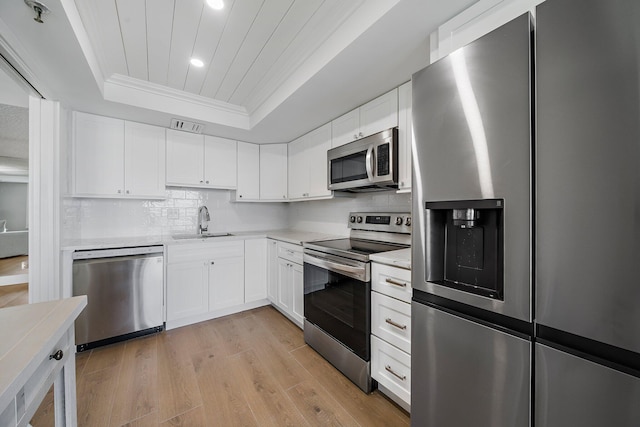 kitchen featuring appliances with stainless steel finishes, a tray ceiling, white cabinetry, and light hardwood / wood-style floors