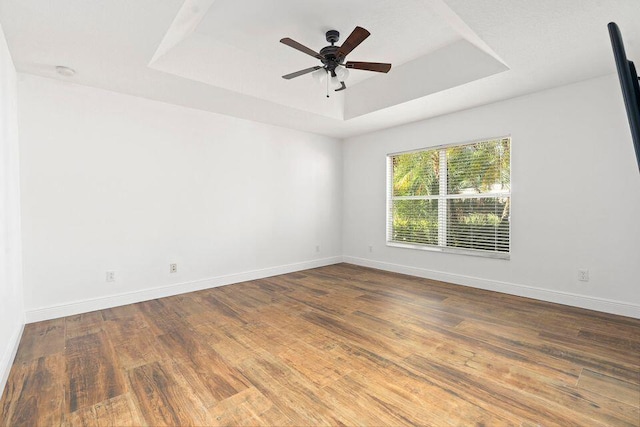 empty room with a tray ceiling, ceiling fan, and hardwood / wood-style floors