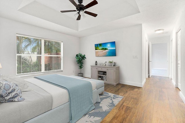 bedroom with ceiling fan, a tray ceiling, and light hardwood / wood-style flooring