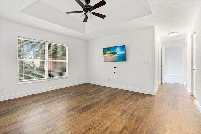 empty room featuring a raised ceiling, ceiling fan, and dark hardwood / wood-style flooring