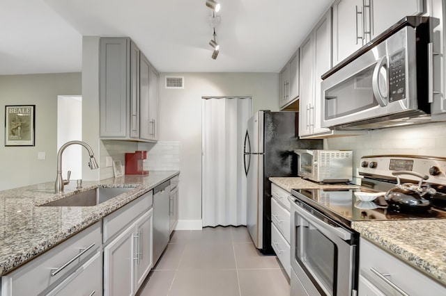 kitchen featuring light stone countertops, appliances with stainless steel finishes, rail lighting, sink, and light tile patterned floors