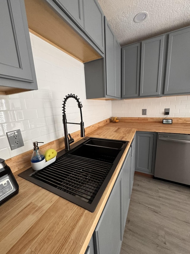 kitchen with gray cabinetry, dishwasher, sink, butcher block countertops, and decorative backsplash