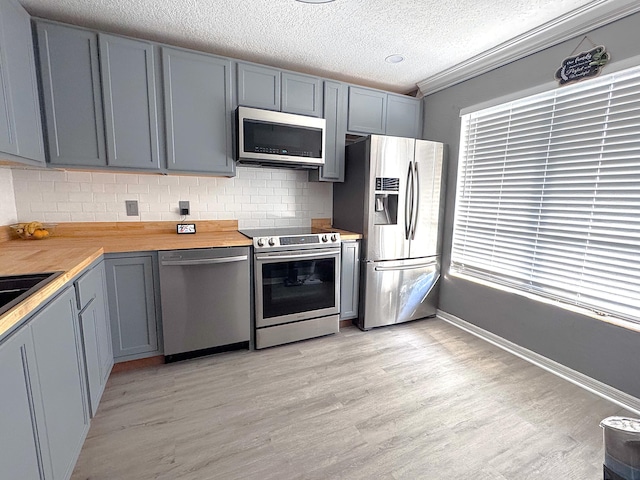 kitchen featuring wood counters, light hardwood / wood-style flooring, backsplash, gray cabinets, and appliances with stainless steel finishes