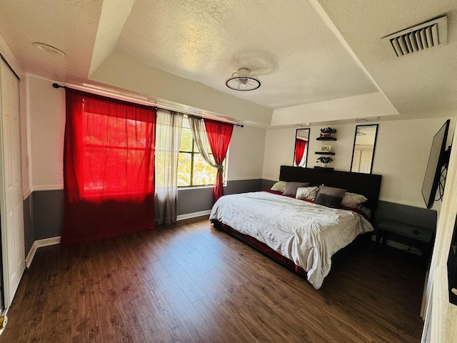 bedroom featuring a raised ceiling, dark hardwood / wood-style flooring, and a textured ceiling