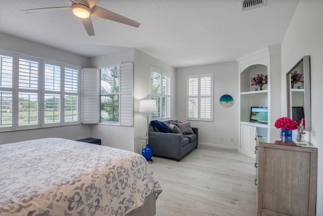 bedroom featuring ceiling fan, light wood-type flooring, a textured ceiling, and multiple windows