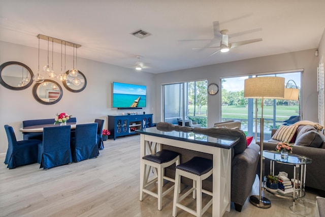 kitchen with a breakfast bar, hanging light fixtures, ceiling fan with notable chandelier, and light wood-type flooring