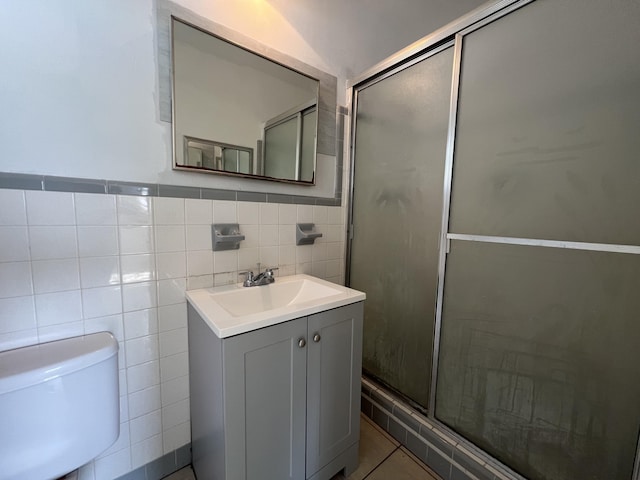 bathroom with tile patterned flooring, tile walls, vanity, a shower with shower door, and toilet