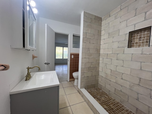 bathroom with a shower, tile walls, vanity, toilet, and tile patterned floors