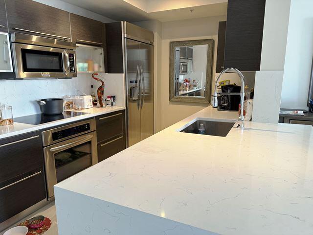 kitchen with sink, decorative backsplash, appliances with stainless steel finishes, light stone counters, and dark brown cabinetry