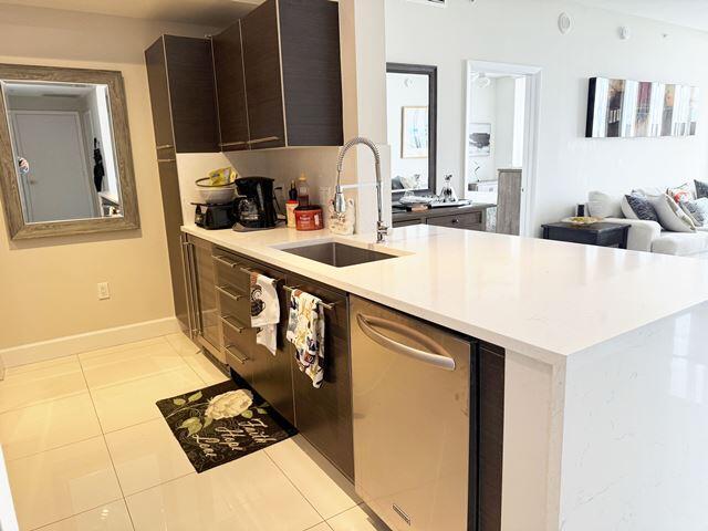 kitchen featuring dark brown cabinetry, sink, stainless steel dishwasher, kitchen peninsula, and light tile patterned floors