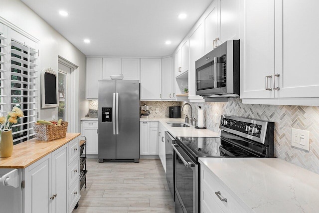 kitchen with backsplash, sink, light hardwood / wood-style floors, white cabinetry, and stainless steel appliances