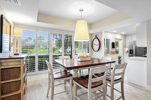 dining space with a raised ceiling and light hardwood / wood-style flooring