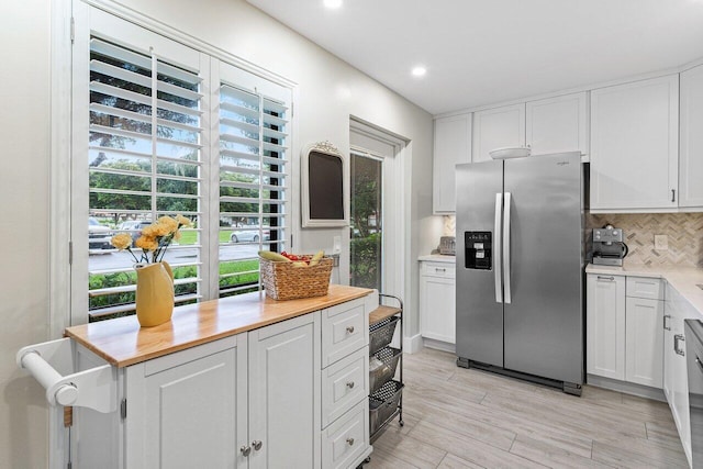 kitchen featuring stainless steel refrigerator with ice dispenser, backsplash, light hardwood / wood-style floors, and white cabinetry