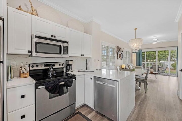 kitchen with white cabinets, ornamental molding, kitchen peninsula, and appliances with stainless steel finishes