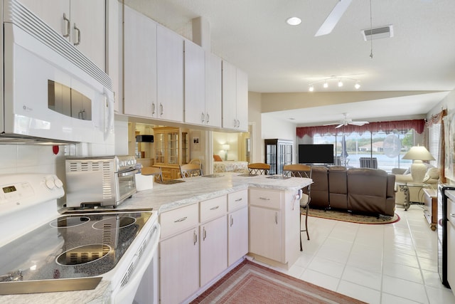 kitchen with lofted ceiling, white cabinetry, electric stove, and kitchen peninsula