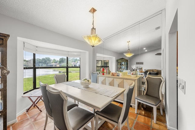 tiled dining space featuring lofted ceiling, a water view, and a textured ceiling