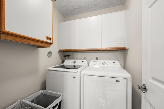 clothes washing area with washing machine and clothes dryer, cabinets, and a textured ceiling