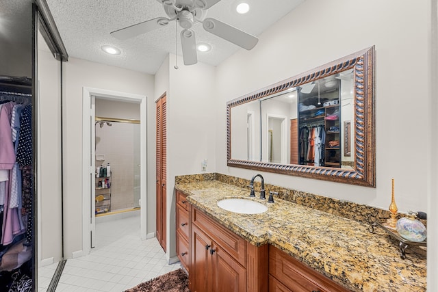 bathroom featuring ceiling fan, tile patterned flooring, a textured ceiling, an enclosed shower, and vanity