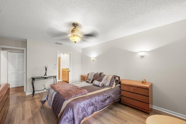 bedroom with ensuite bath, a textured ceiling, ceiling fan, light hardwood / wood-style floors, and a closet