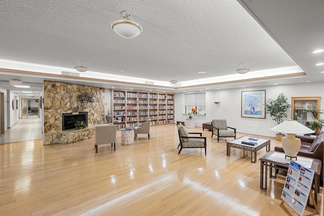 living room with a tray ceiling, a fireplace, a textured ceiling, and light hardwood / wood-style flooring